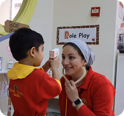 Child and adult woman in red shirts engaging in role play with a toy telephone at a classroom play area.