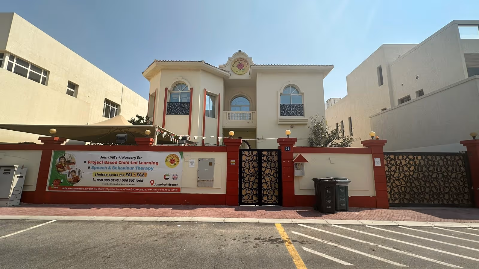Two-story beige nursery building with red pillars and a banner promoting project-based child-led learning and speech therapy services.