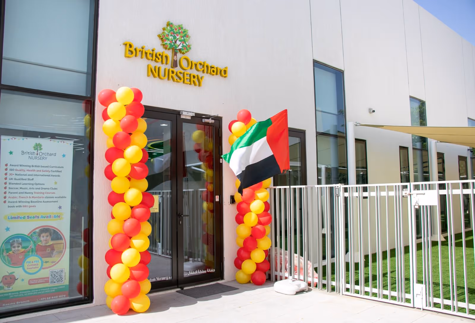 Entrance of British Orchard Nursery decorated with red and yellow balloons and a UAE flag beside the door.