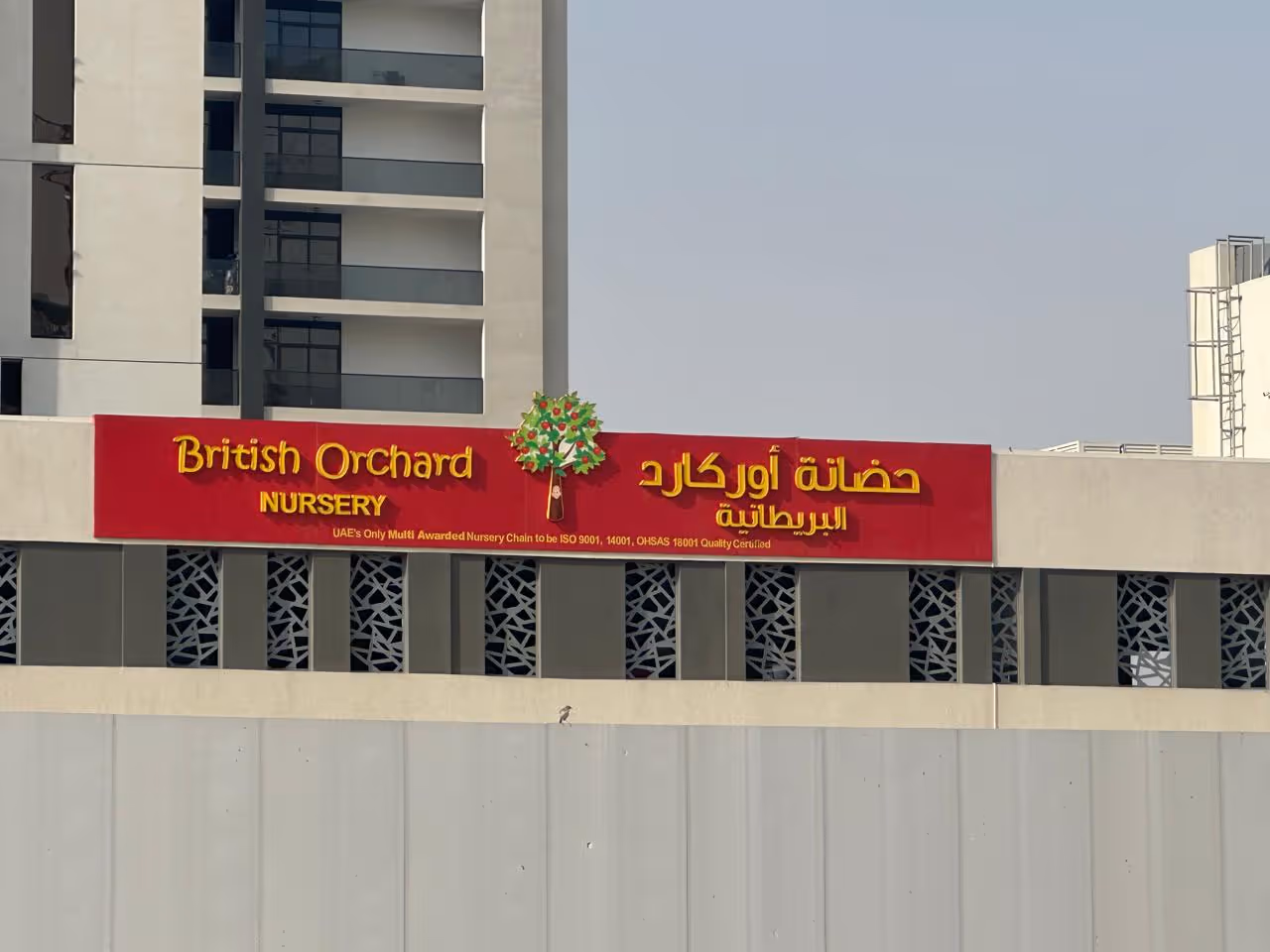 Red sign for British Orchard Nursery with yellow text and a tree logo on a building facade.