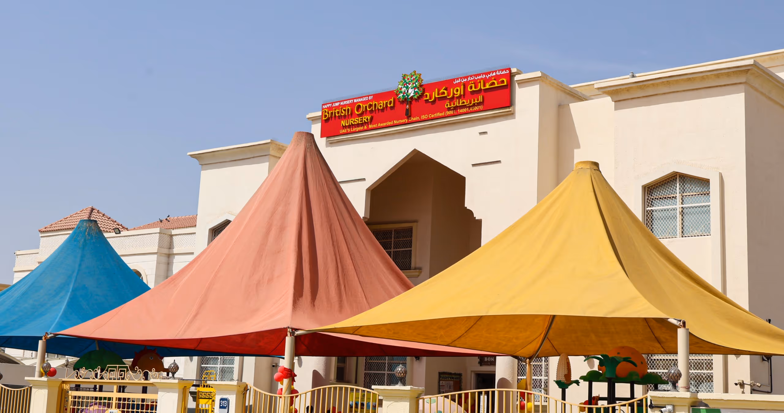 British Orchard Nursery building with colorful orange, blue, and yellow canopy tents outside under a clear sky.