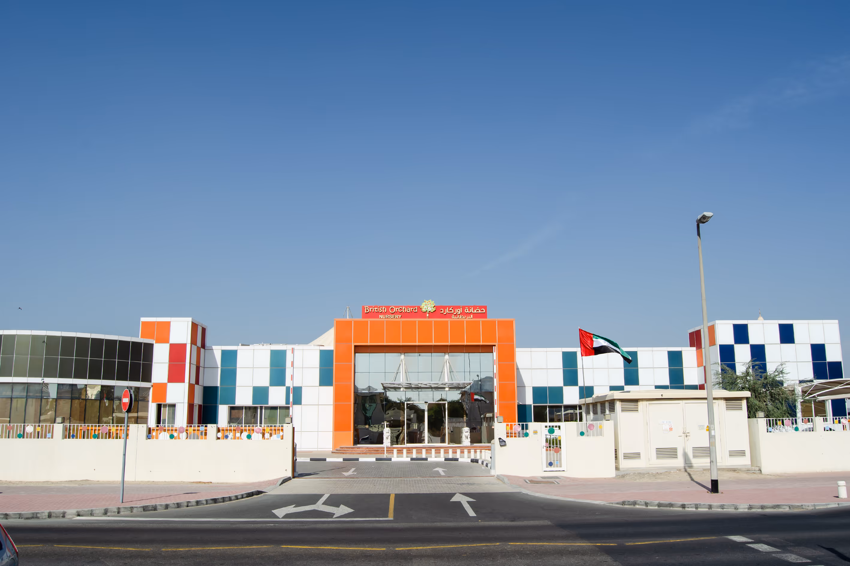 Front view of British Orchard Nursery building with orange and blue checkered facade and UAE flag on the right.