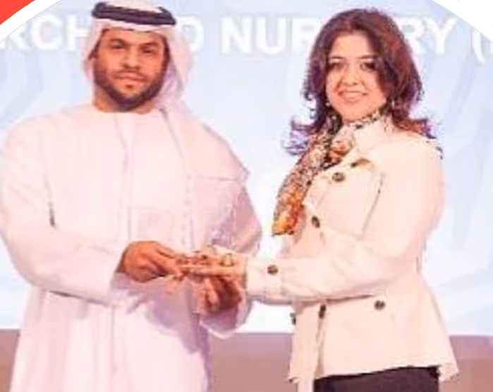 Man in traditional Middle Eastern attire receiving an award from a woman in a white jacket and patterned scarf on a stage.