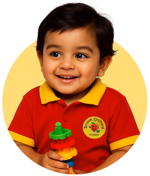 Smiling toddler in British Orchard Nursery red and yellow uniform holding colorful toy blocks.
