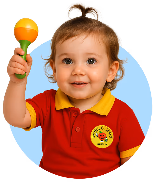 Toddler wearing British Orchard Nursery red and yellow uniform, holding up a green and orange toy maraca and smiling.