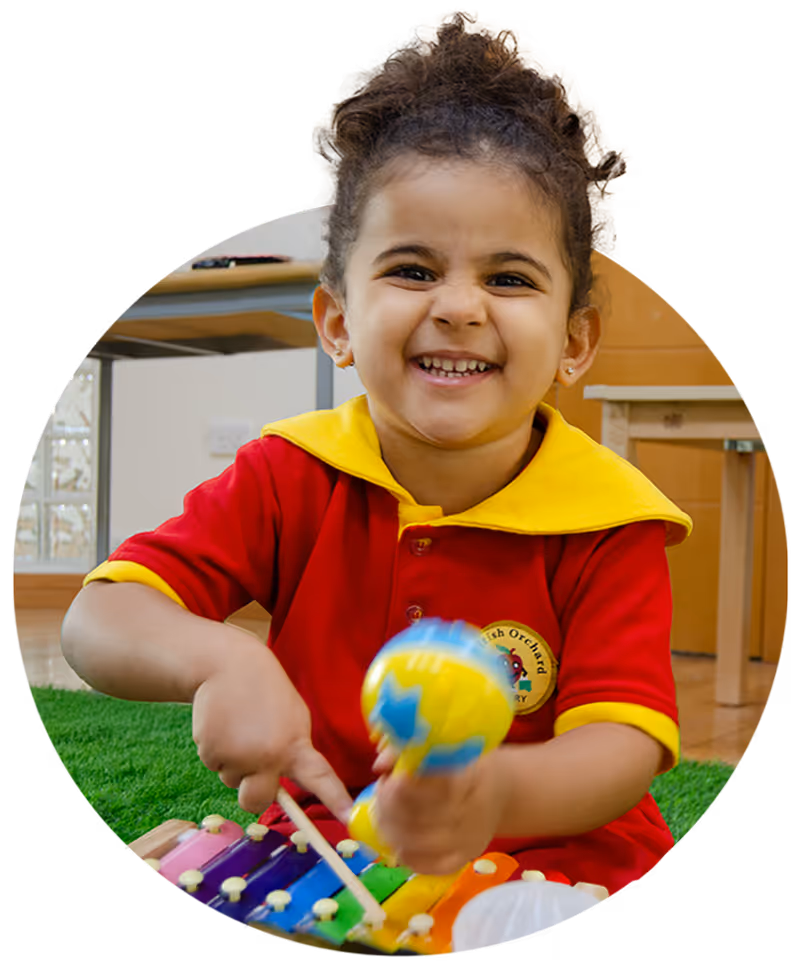 Young child smiling and playing a colorful xylophone while holding a maraca.