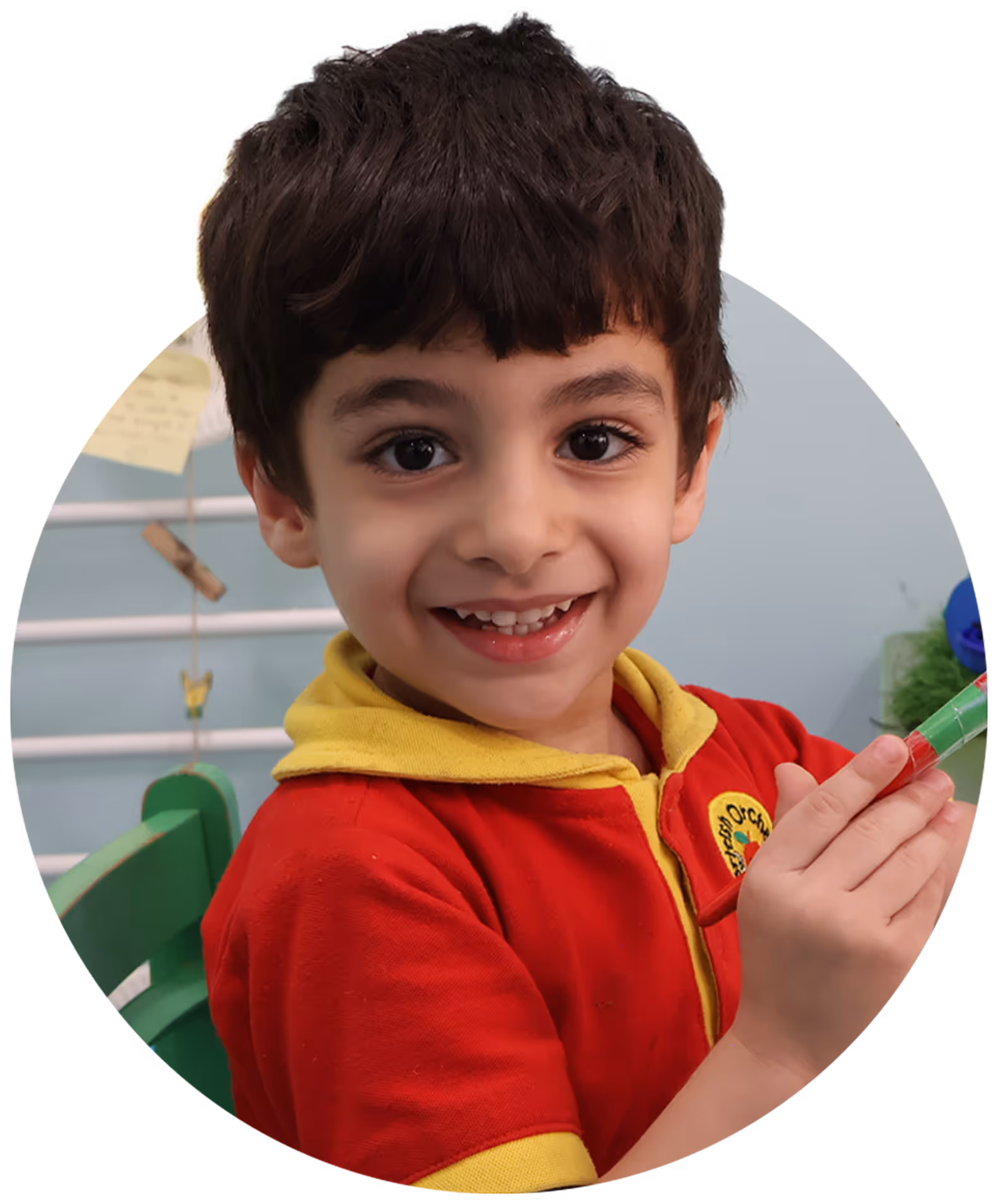 Smiling young boy with dark hair wearing a red and yellow shirt holding a green and red marker.
