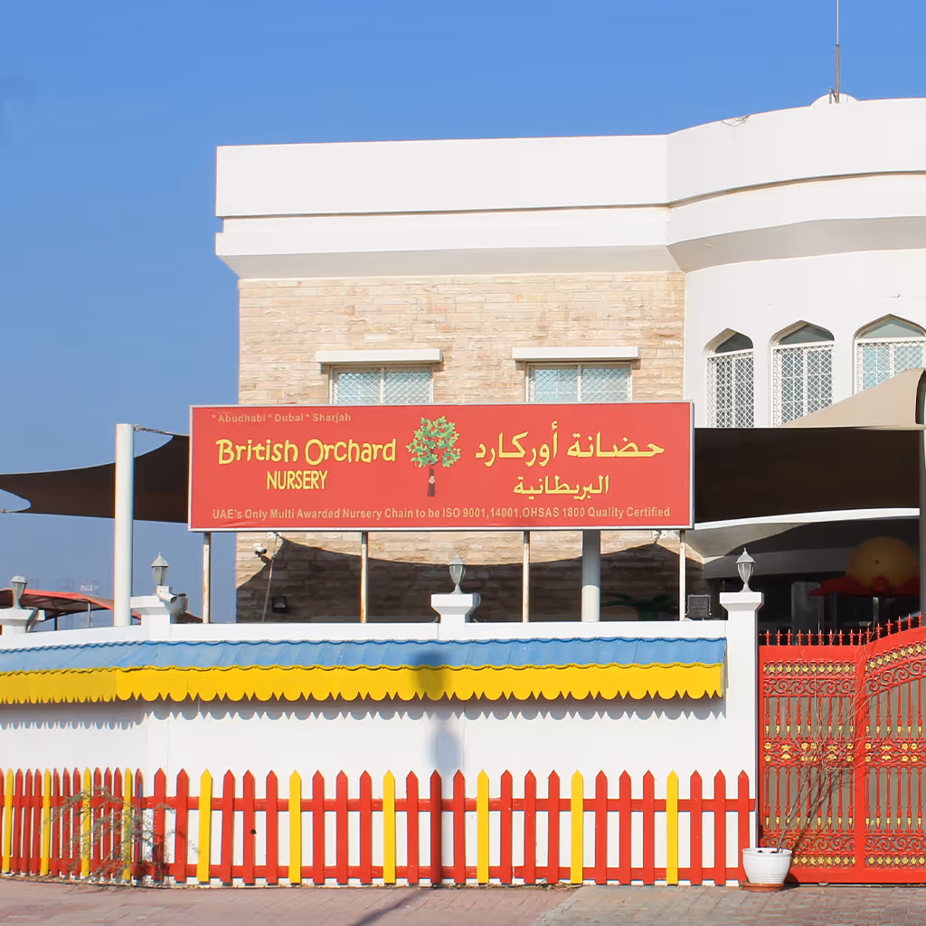 British Orchard Nursery building with red and yellow picket fence and red signage against a clear blue sky.