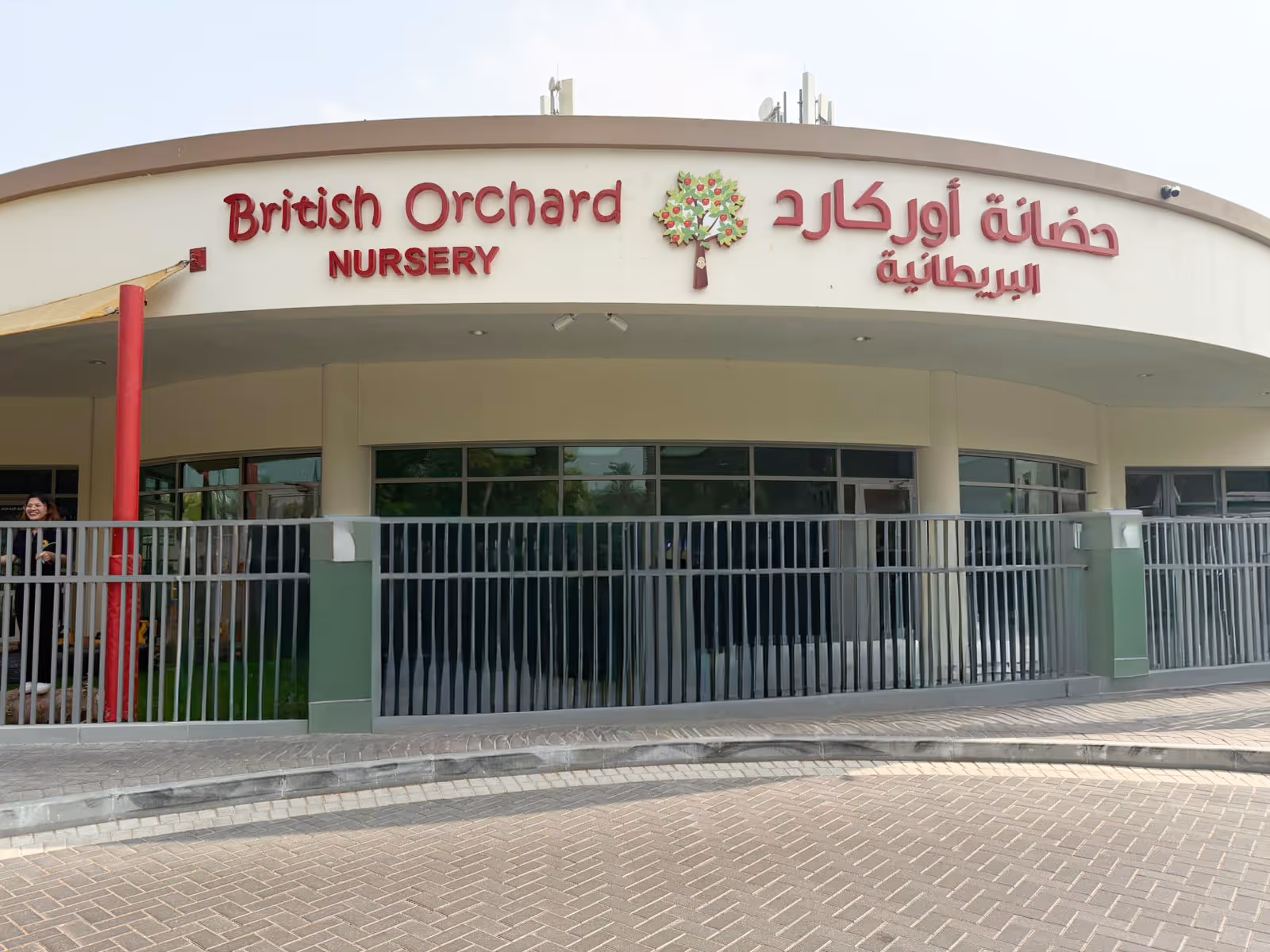 Exterior view of British Orchard Nursery building with signage in English and Arabic and a tree logo above the entrance.