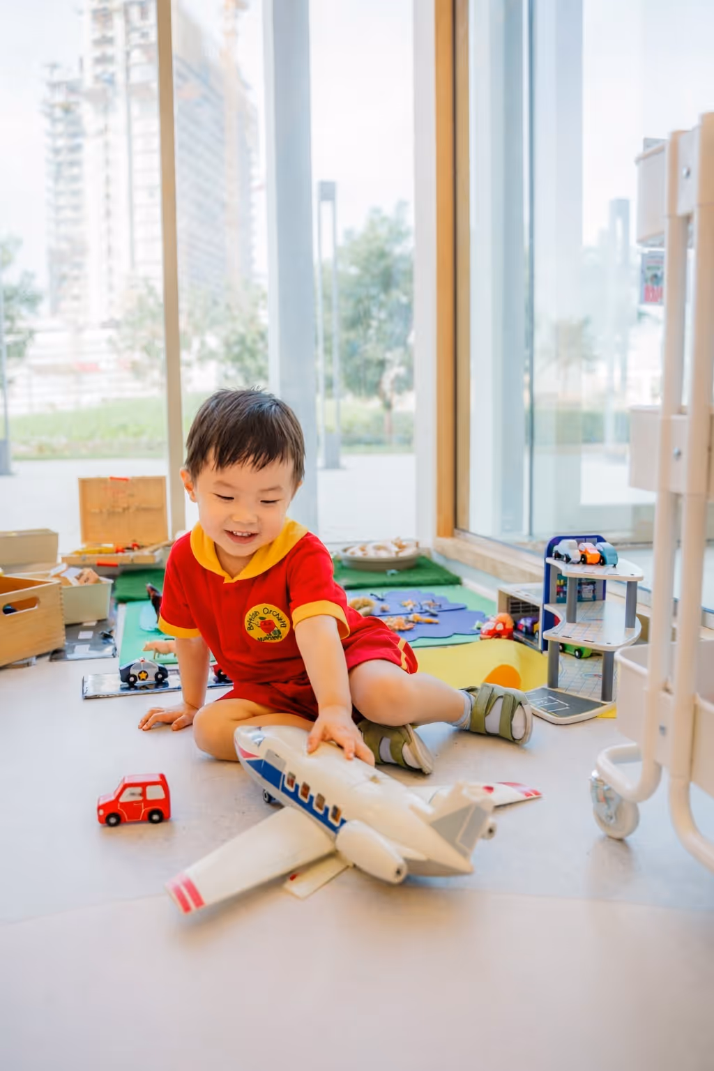 Young child sitting on the floor indoors playing with a large toy airplane surrounded by other toys.