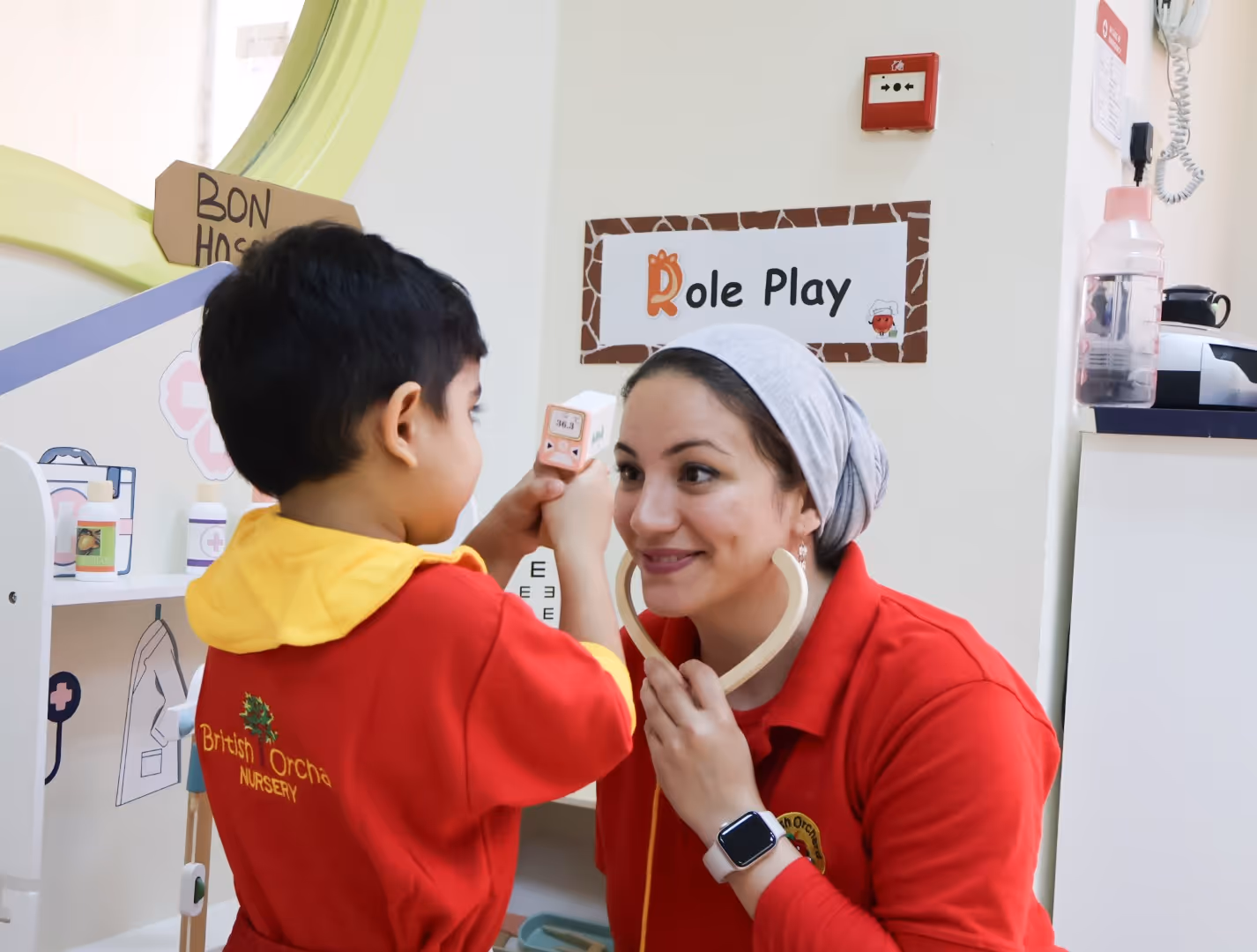 Child and adult woman engaged in role play, with the adult holding a toy stethoscope and the child holding a toy thermometer.