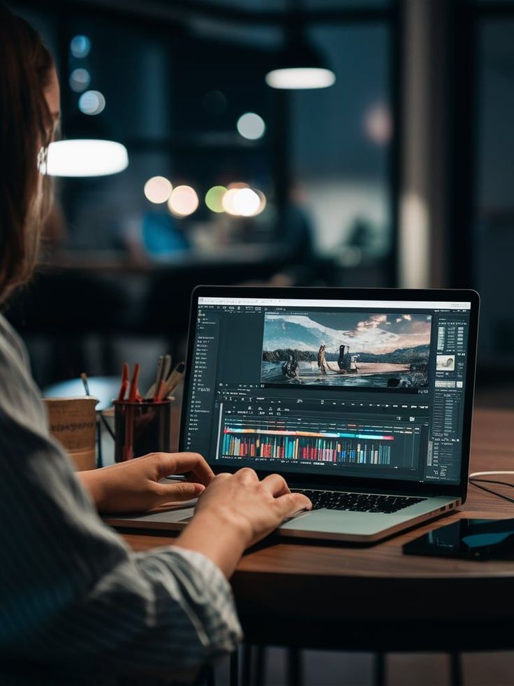 This may contain: a woman sitting at a table with a laptop on her lap looking at the screen