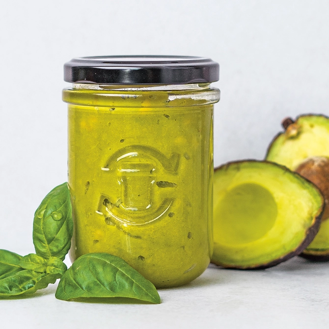 Grüner Aufstrich in einem Schraubglas mit frischem Basilikum und Avocado dekoriert