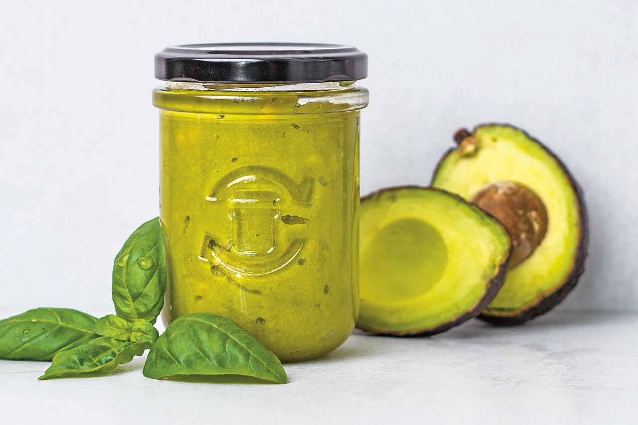 Grüner Aufstrich in einem Schraubglas mit frischem Basilikum und Avocado dekoriert