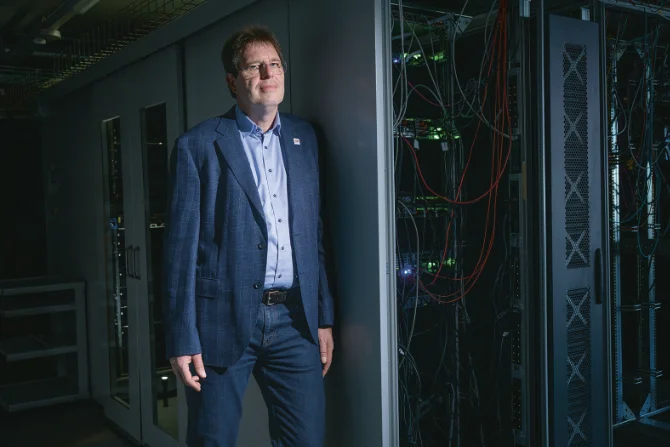 Mann steht neben Server-Schränken in einem dunklen Serverraum