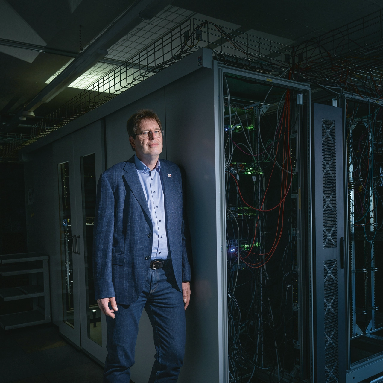 Mann steht neben Server-Schränken in einem dunklen Serverraum