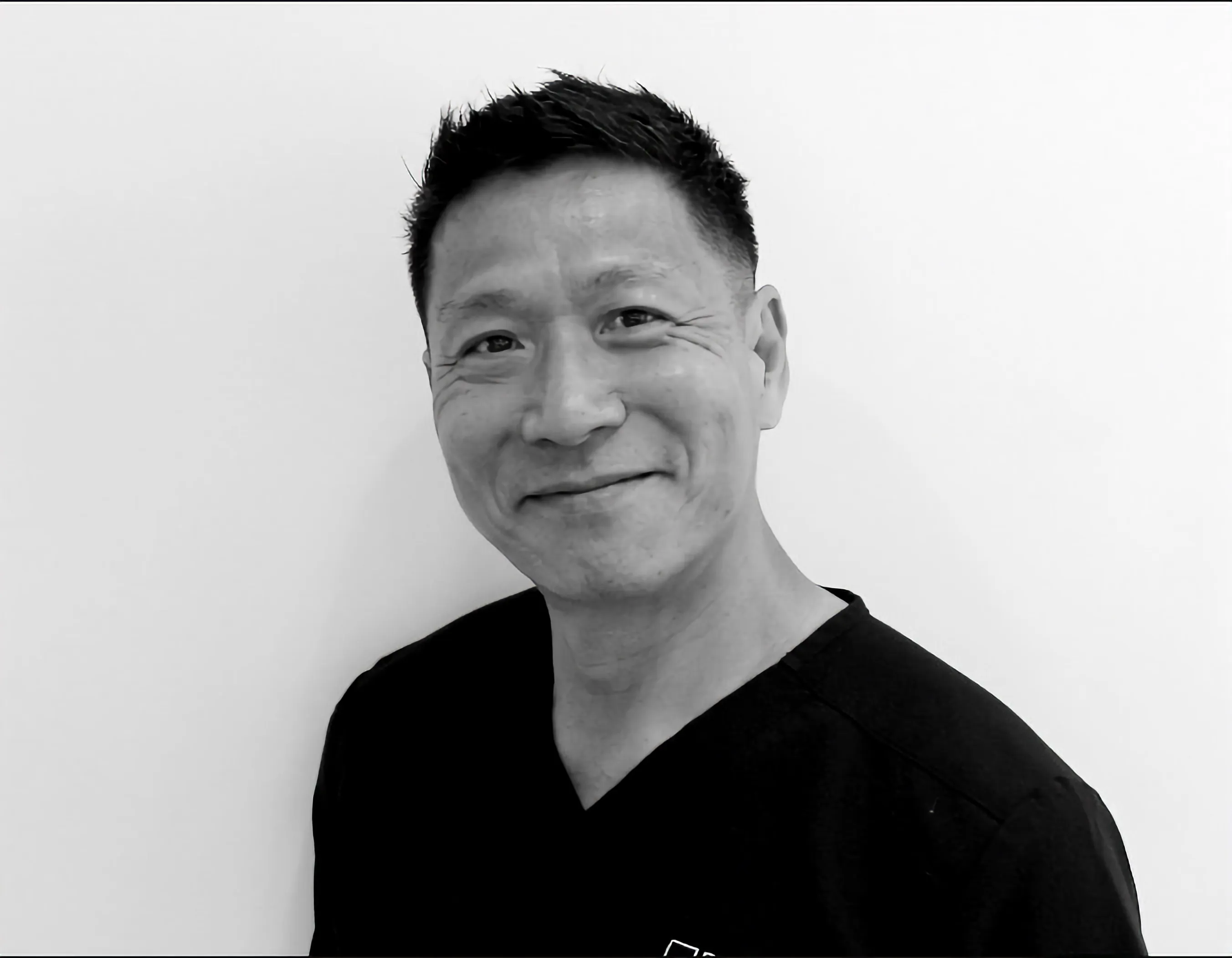 Smiling man with short black hair wearing a black shirt against a white background.