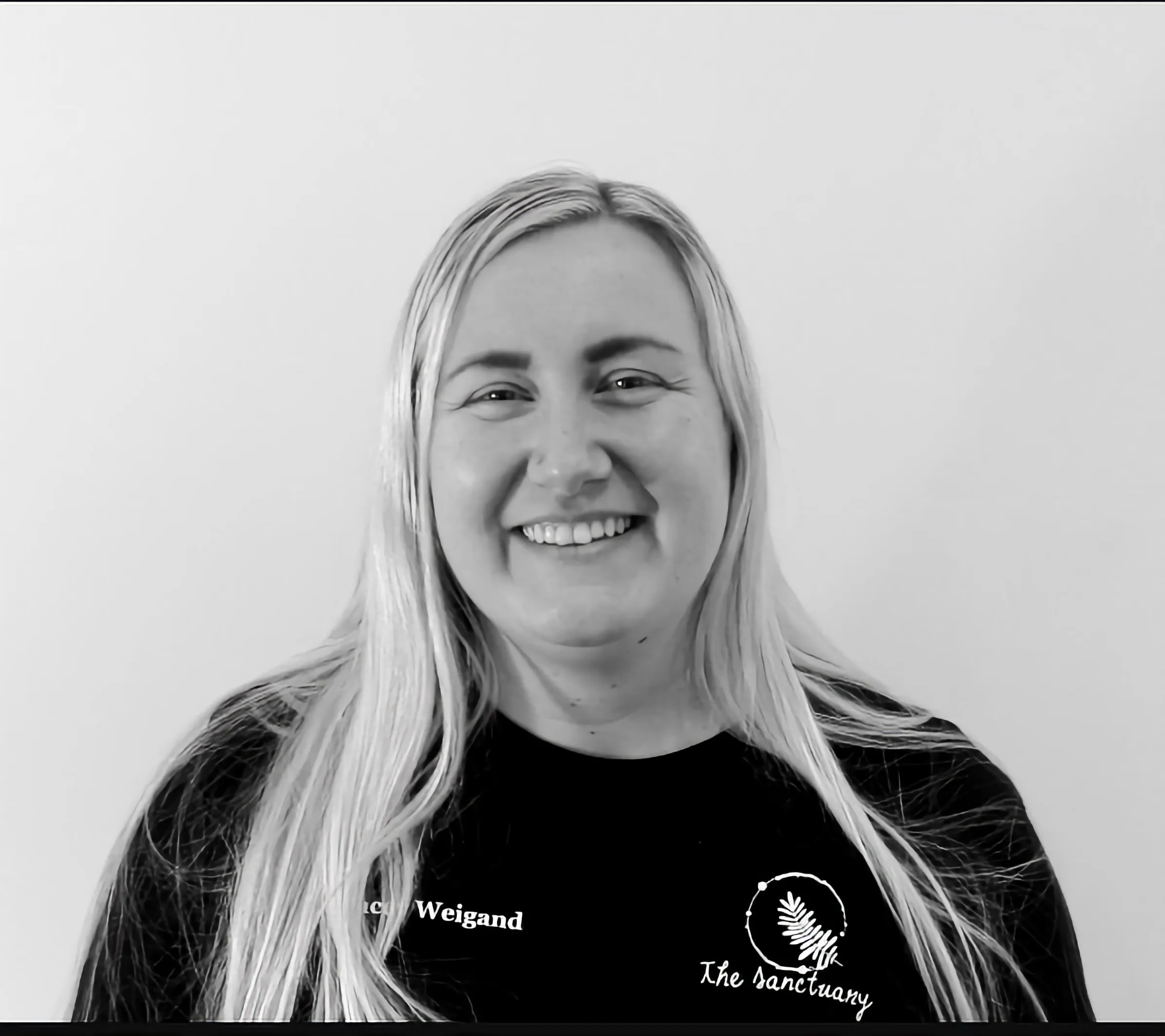 Smiling woman with long blonde hair wearing a black shirt with The Sanctuary logo.