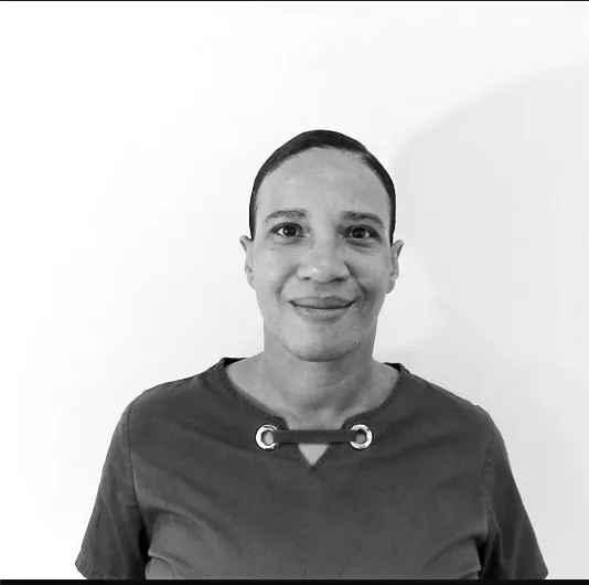 Smiling person with short hair wearing a dark shirt with metal ring details on the neckline.