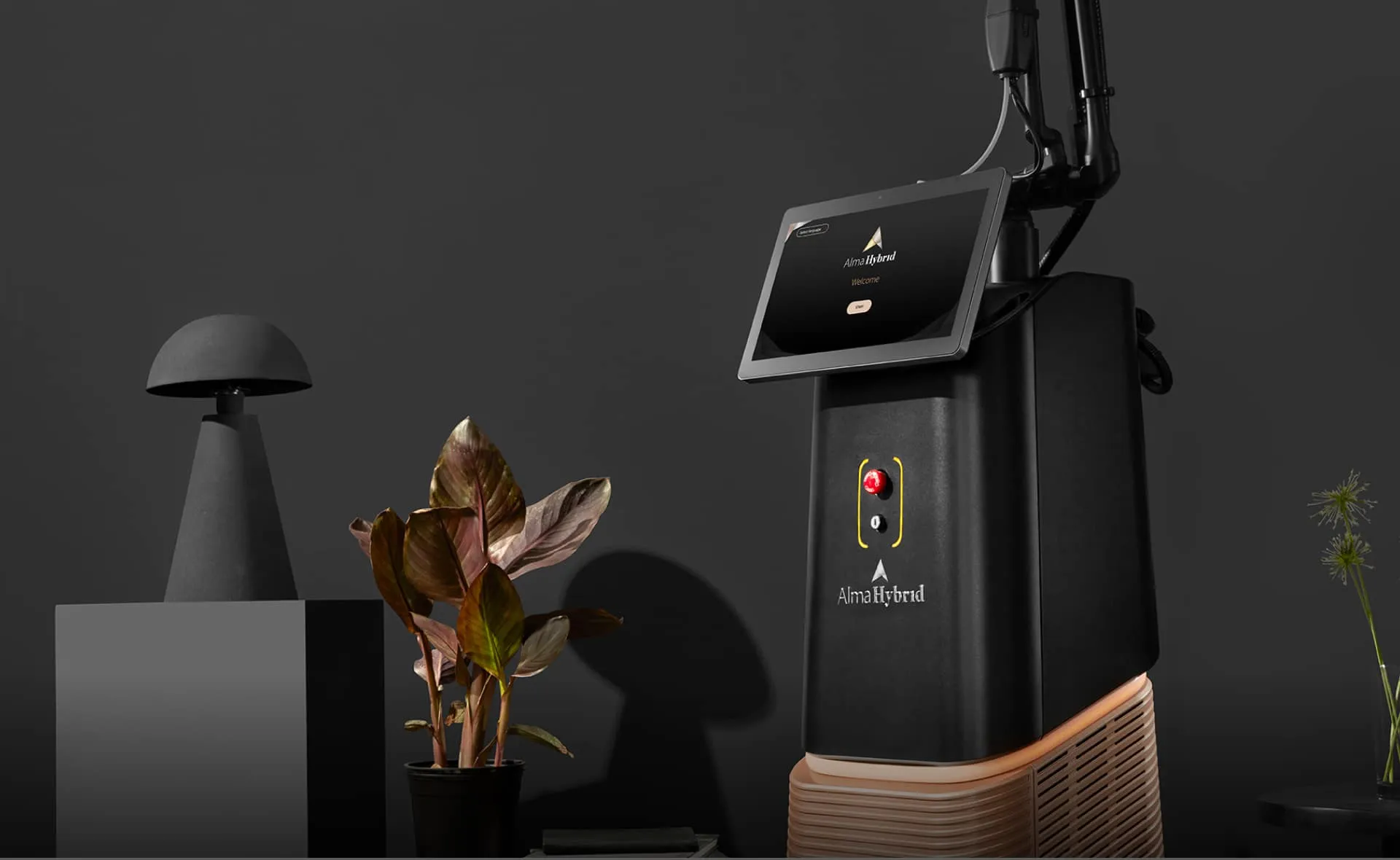 Black Alma Hybrid device with touchscreen and buttons next to a potted plant and modern black lamp.