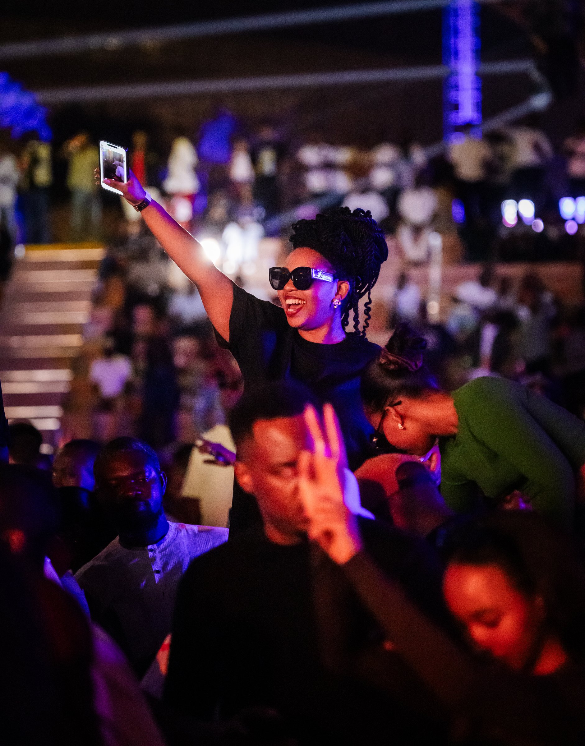 Fan cheering and raising her phone in the crowd at a Zaria Court Kigali event