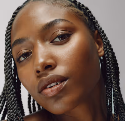 Close-up of a young woman with smooth skin and braided hair looking into the camera.