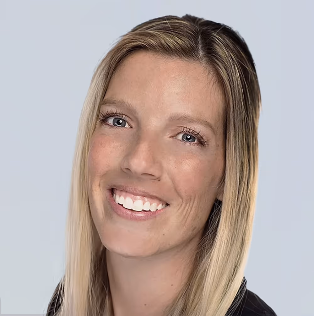 Smiling woman with straight blonde hair and blue eyes against a plain light background.