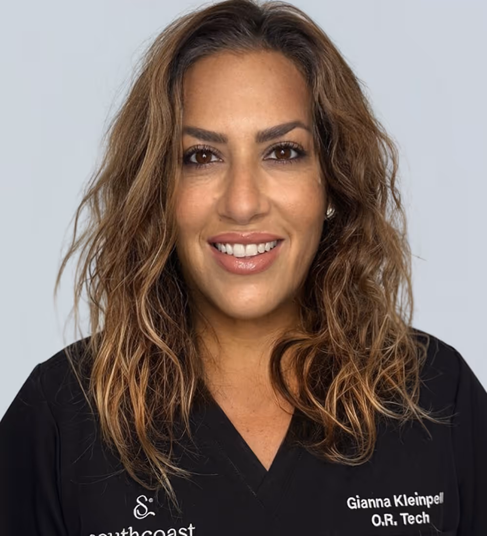 Woman with wavy brown hair smiling, wearing a black shirt with the name Gianna Kleinpell and O.R. Tech embroidered.