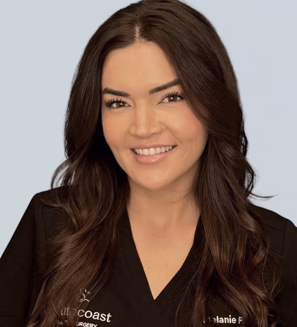 Smiling woman with long brown hair wearing a black medical uniform with 'South Coast Plastic Surgery' and name embroidery.