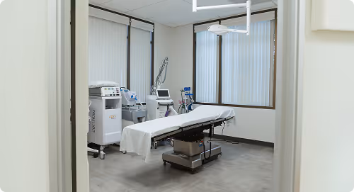 Medical examination room with a treatment table covered in white sheets and various medical equipment against the walls.