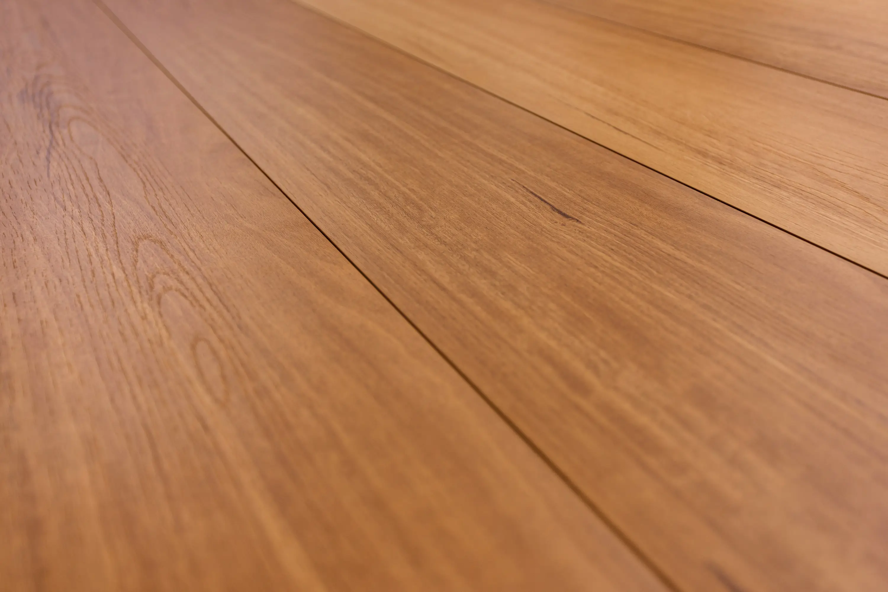 Laminate flooring in a warm honey-brown shade with a smooth matte finish and natural wood grain texture, designed for a stylish and durable surface.