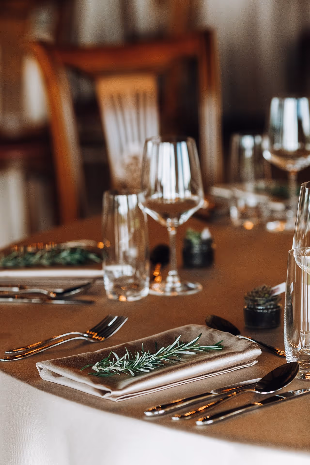 Elegant dining table set with silverware, glassware, and a napkin featuring a sprig of rosemary for decoration.
