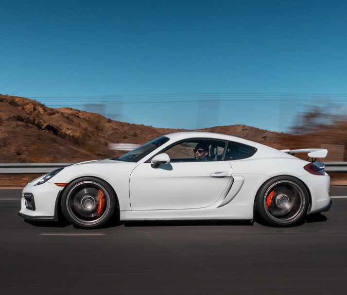 Alex Lawson kneeling beside his Porsche Cayman GT4 with the door panel removed
