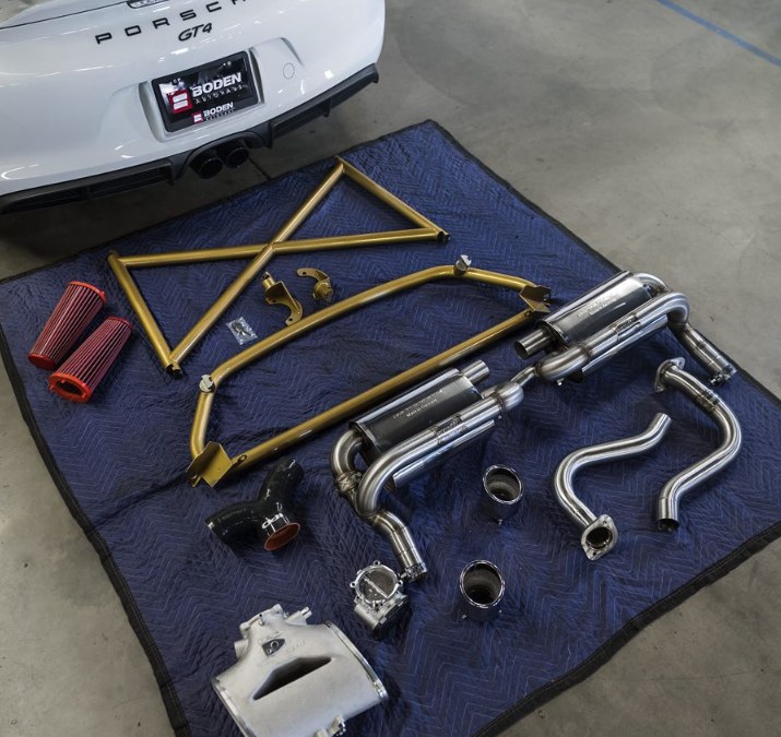 Roll bar, exhaust and intake parts laid out behind a Porsche Cayman GT4 before installation