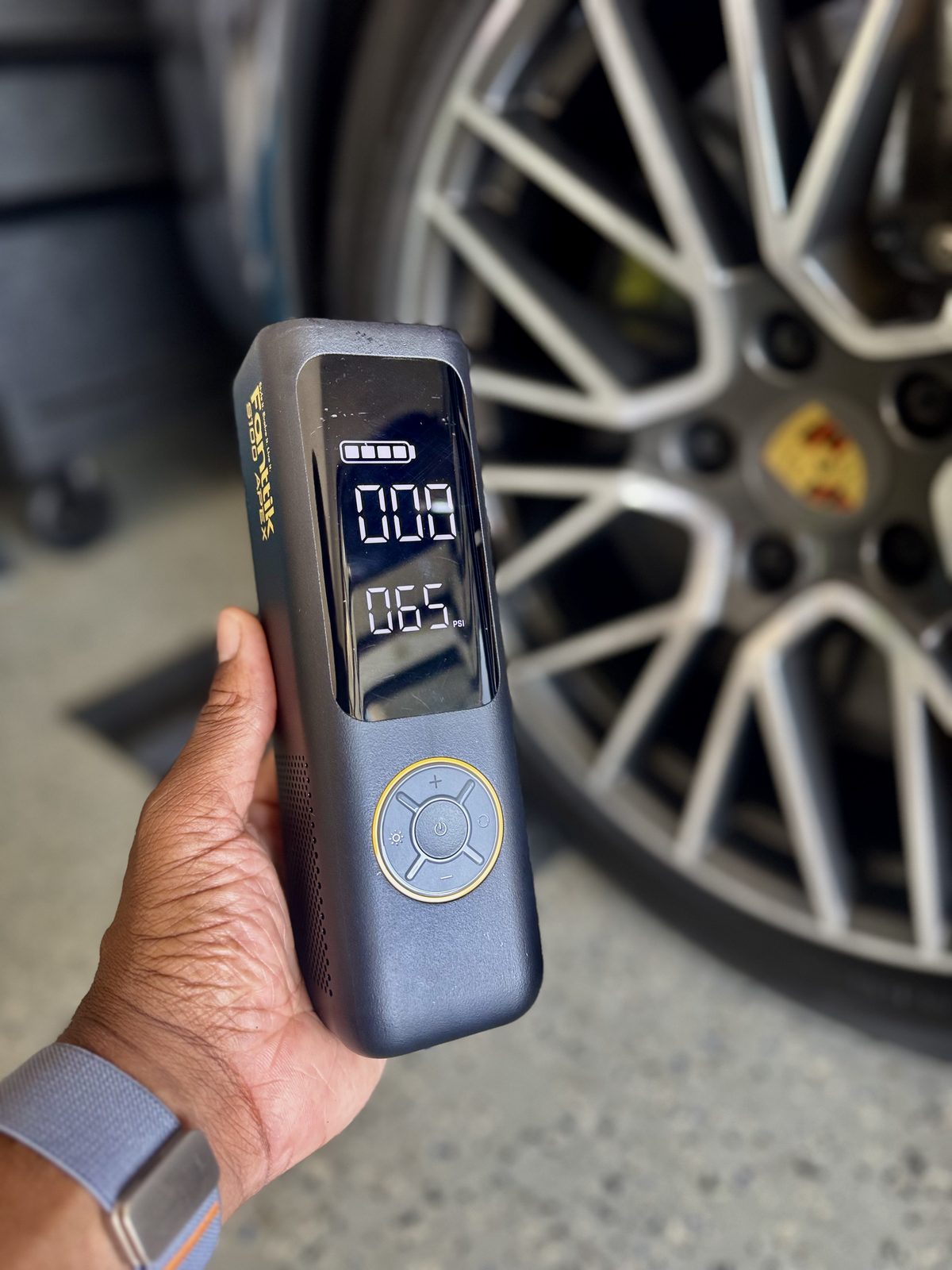 Holding the Fanttik X8 Apex tire inflator in front of a Porsche wheel in a home garage