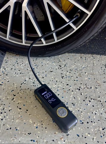 Fanttik X8 Apex connected to a car tire valve stem on a garage floor with the screen showing PSI