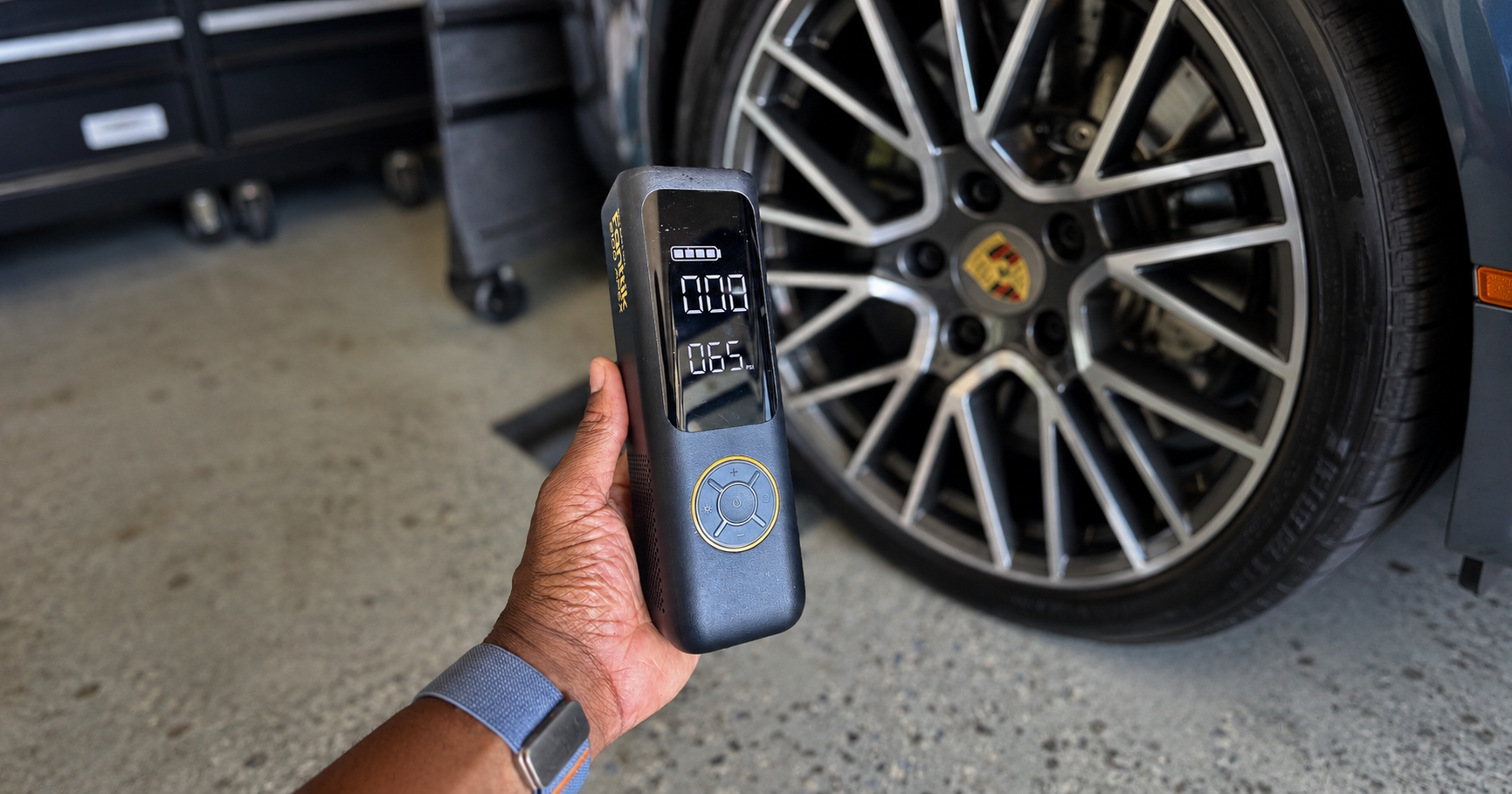 The Fanttik X8 Apex in a user's hand in a garage next to a Porsche GT4