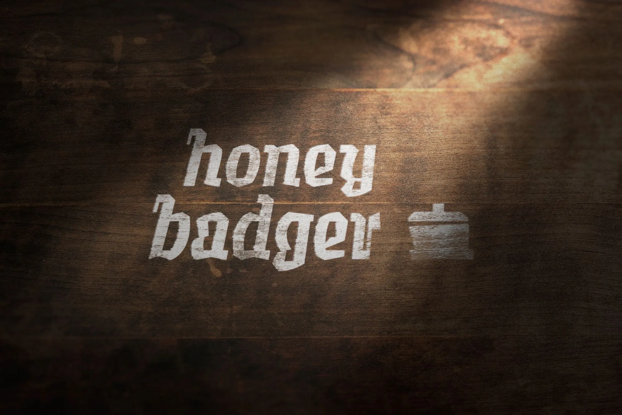 The Honey Badger logo and pot icon painted in white on a dark wooden surface, with soft lighting casting a warm shadow.