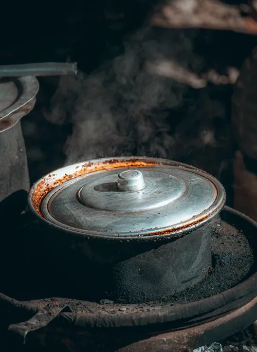 A well-used metal pot with a lid steaming over a traditional stove, symbolizing rustic and hearty cooking.