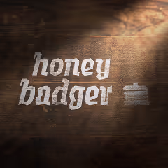 The Honey Badger logo and pot icon painted in white on a dark wooden surface, with soft lighting casting a warm shadow.