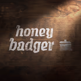 The Honey Badger logo and pot icon painted in white on a dark wooden surface, with soft lighting casting a warm shadow.