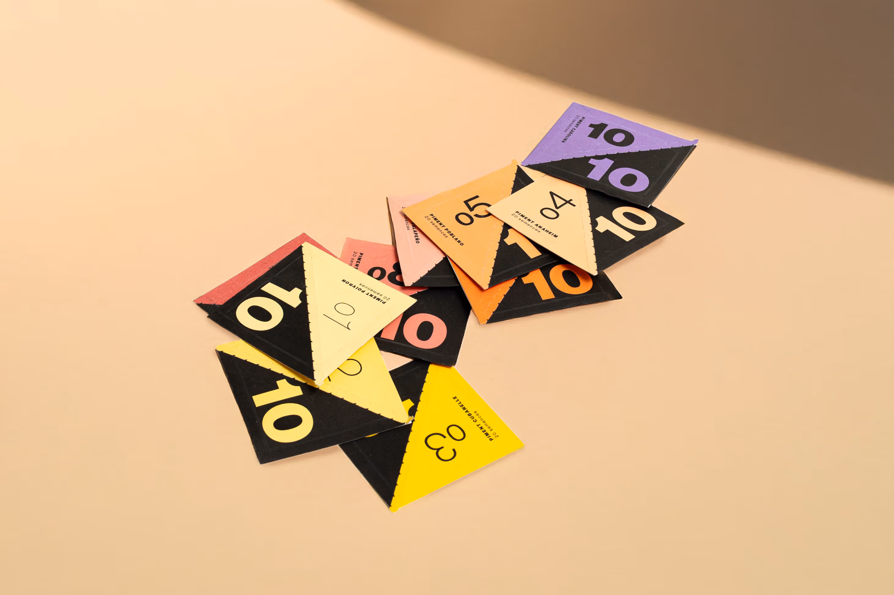 A variety of triangular pepper seed packets scattered on a white background, showing their vivid gradient color scheme.