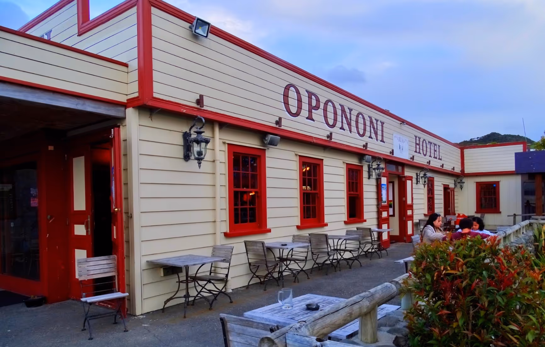 Exterior view of a cozy restaurant with red accents and outdoor seating, set against a colorful evening sky.