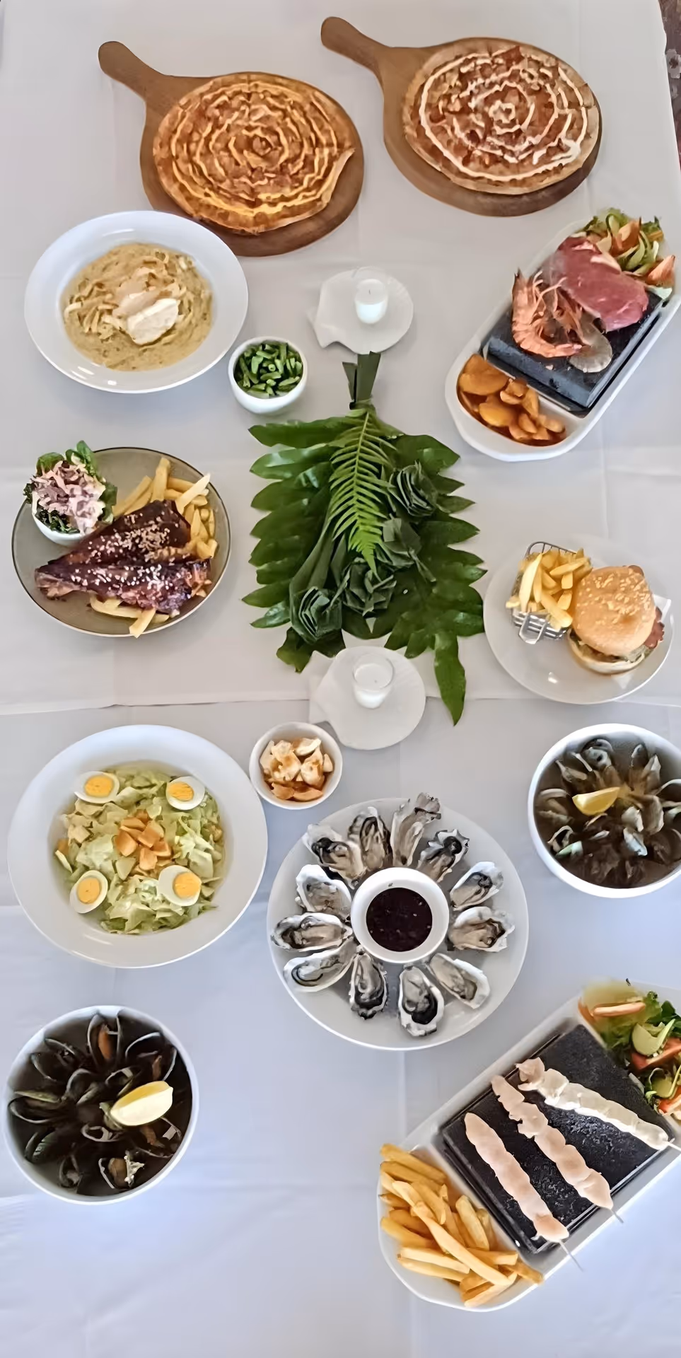 A variety of dishes including pizzas, salads, meats, and sides arranged aesthetically on a table, garnished with greenery.