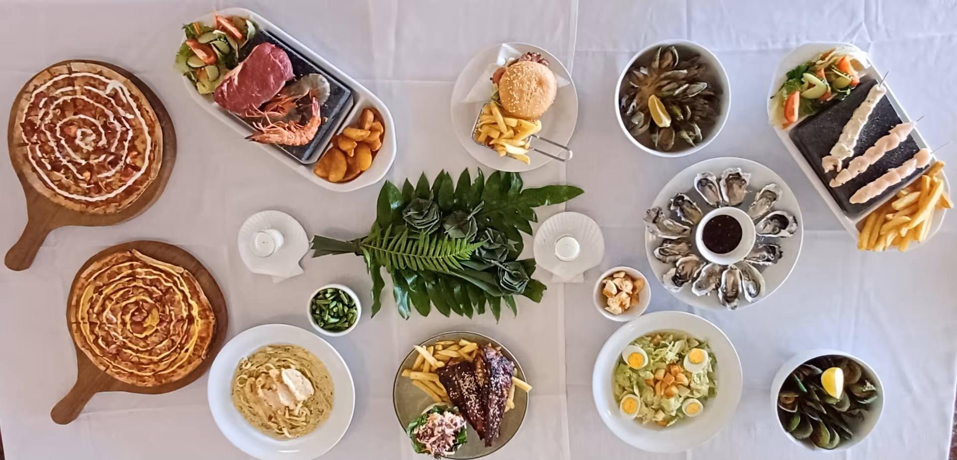 An overhead view of a vibrant table spread featuring various dishes, including pizza, seafood, salads, and garnishes.