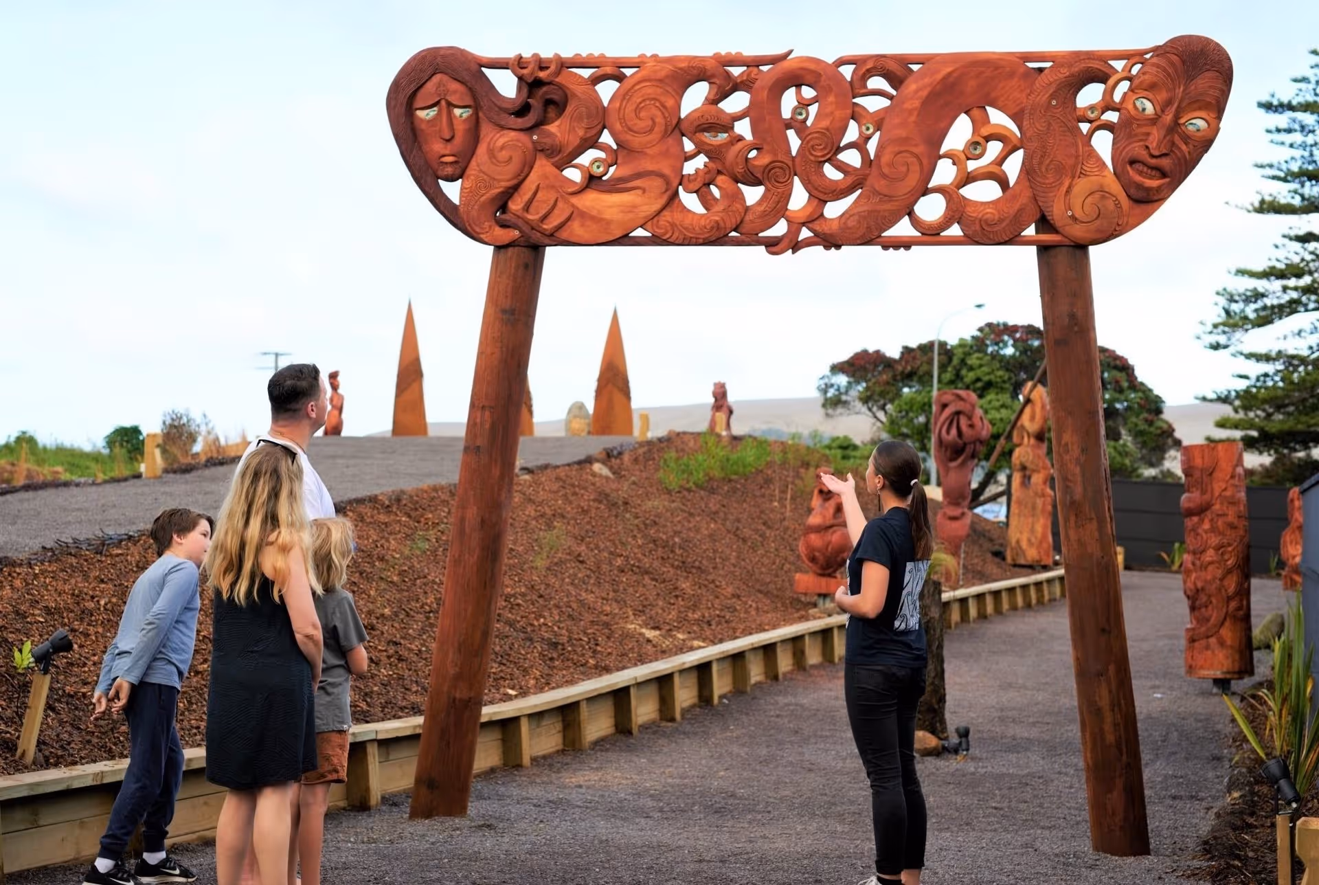 Visitors admire a large carved wooden gateway adorned with intricate patterns, set in a scenic outdoor area.