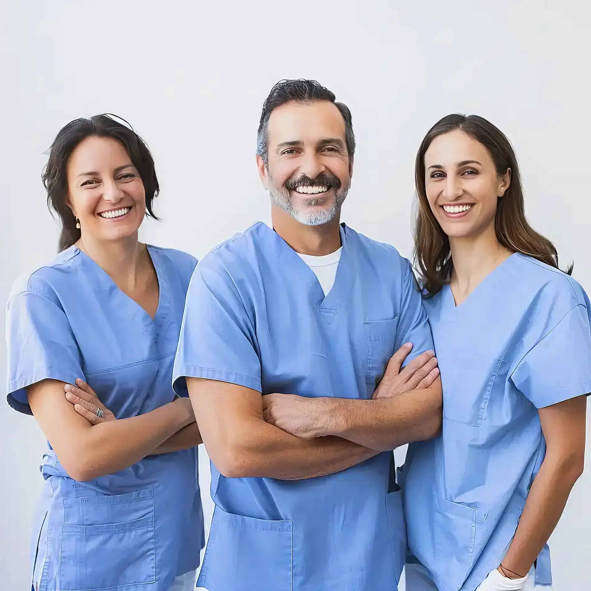 Three smiling medical professionals in blue scrubs standing with arms crossed against a plain background.