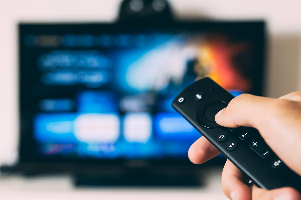 Hand holding a streaming remote in front of a TV