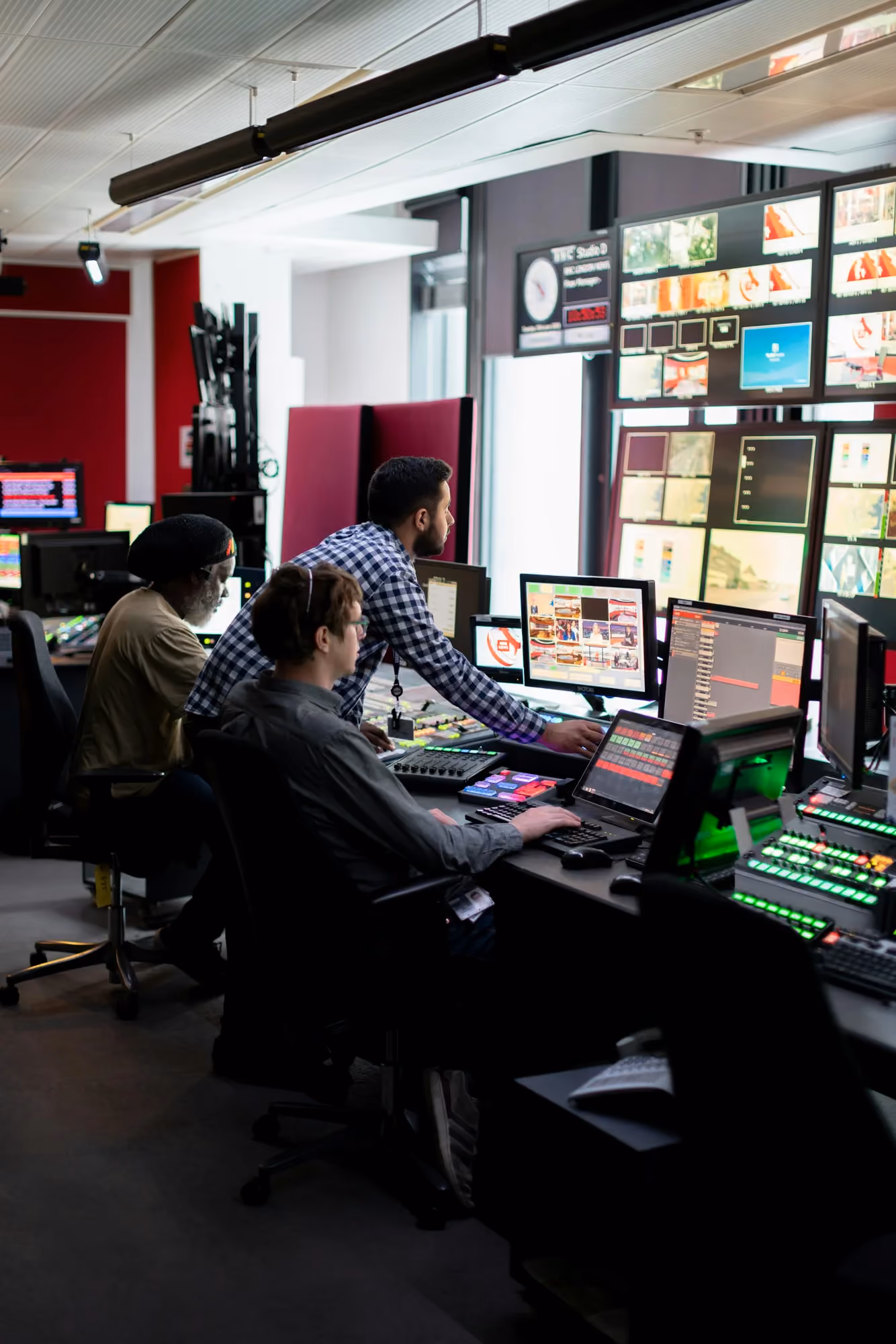 Media team working in a broadcast control room in front of a wall of screens