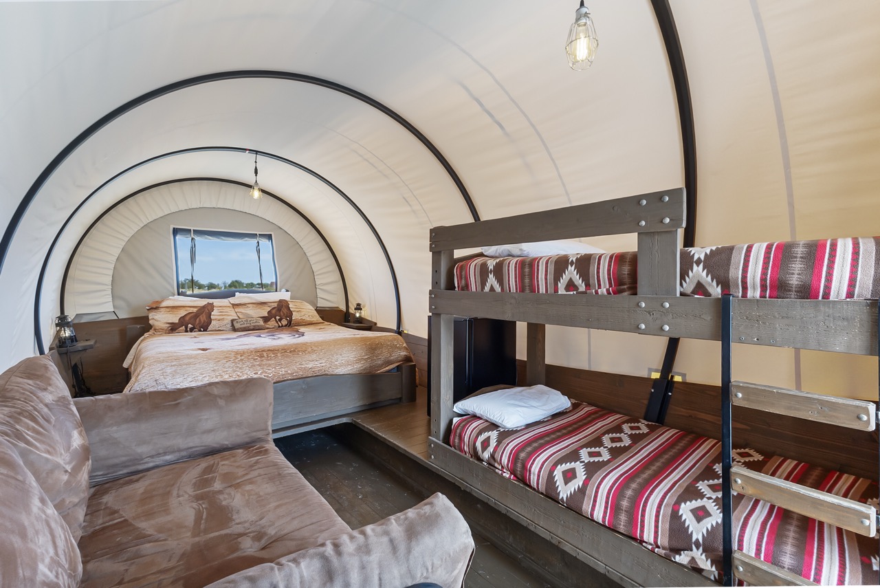 Interior of a Conestoga wagon at Broken Spur Inn near Capitol Reef National Park, featuring a queen bed, bunk beds, and Western-style decor.